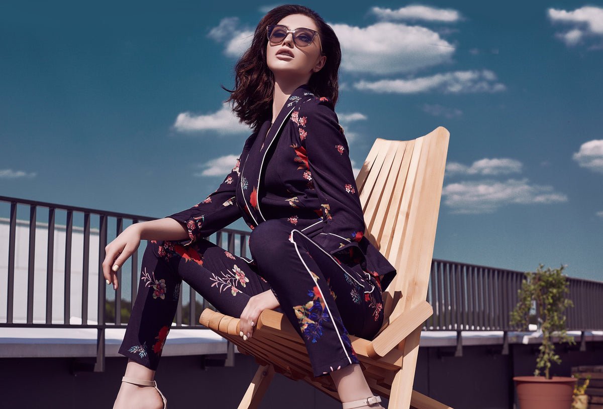 Woman in elegant floral patterned outfit sitting on modern chair against blue sky